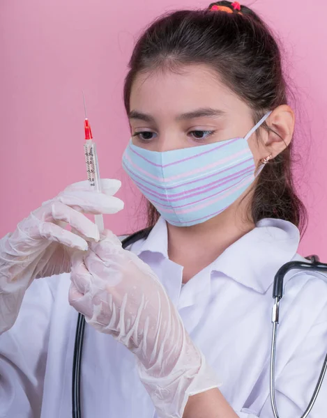 Doktor üniforması giyerken steteskopu ve şırıngası olan komik bir kız. Renkli maskeli Asyalı kız