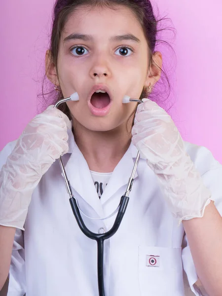 Little funny girl with a collorful stethoscope while wearing Doctor\'s uniform. Excitement and fascination concept. Coronavirus background. foolish grimaces comical crazy gestur.  Funny expression.