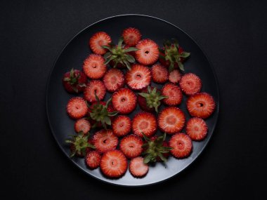 Çilekli kadın doğum siyah tabağı. Siyah arka planda meyve, siyah tabakta kiraz eriği ve çilek.