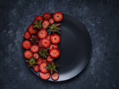 Çilekli kadın doğum siyah tabağı. Siyah arka planda meyve, siyah tabakta kiraz eriği ve çilek.