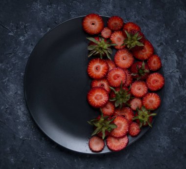 Çilekli kadın doğum siyah tabağı. Siyah arka planda meyve, siyah tabakta kiraz eriği ve çilek.