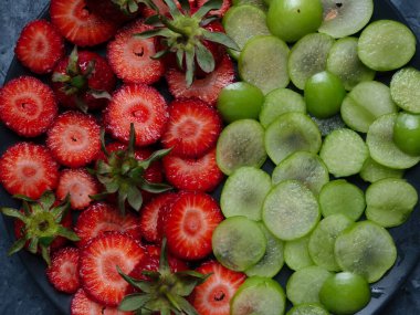 Çilekli kadın doğum siyah tabağı. Siyah arka planda meyve, siyah tabakta kiraz eriği ve çilek.