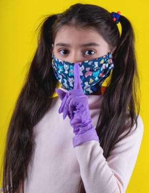 Sarı arka planda steteskop ve maske takan tatlı bir kız. Evde kal. Covid-19 'u durdurun. Virüs koruma ekipmanları. Karantinaya alın. Kız doktoru oynuyor. Eğitim ve işgal konsepti. Kendinde kal.