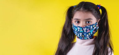 Sarı arka planda steteskop ve maske takan tatlı bir kız. Evde kal. Covid-19 'u durdurun. Virüs koruma ekipmanları. Karantinaya alın. Kız doktoru oynuyor. Eğitim ve işgal konsepti. Kendinde kal.