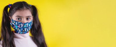 Sarı arka planda steteskop ve maske takan tatlı bir kız. Evde kal. Covid-19 'u durdurun. Virüs koruma ekipmanları. Karantinaya alın. Kız doktoru oynuyor. Eğitim ve işgal konsepti. Kendinde kal.