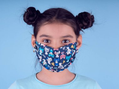 Renkli maskeli komik kız. Heyecan ve cazibe konsepti. Portreyi kapat. Coronavirus 'un mavi arka planı. Aptalca somurtmalar komik çılgın jestler. Komik bir ifade. Covid 19. 