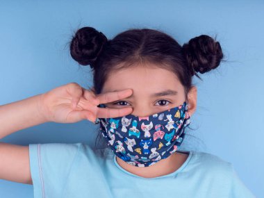 Renkli maskeli komik kız. Heyecan ve cazibe konsepti. Portreyi kapat. Coronavirus 'un mavi arka planı. Aptalca somurtmalar komik çılgın jestler. Komik bir ifade. Covid 19. 