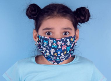 Renkli maskeli komik kız. Heyecan ve cazibe konsepti. Portreyi kapat. Coronavirus 'un mavi arka planı. Aptalca somurtmalar komik çılgın jestler. Komik bir ifade. Covid 19. 