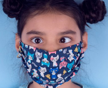 Renkli maskeli komik kız. Heyecan ve cazibe konsepti. Portreyi kapat. Coronavirus 'un mavi arka planı. Aptalca somurtmalar komik çılgın jestler. Komik bir ifade. Covid 19. 