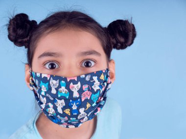 Renkli maskeli komik kız. Heyecan ve cazibe konsepti. Portreyi kapat. Coronavirus 'un mavi arka planı. Aptalca somurtmalar komik çılgın jestler. Komik bir ifade. Covid 19. 