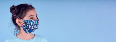 Renkli maskeli komik kız. Heyecan ve cazibe konsepti. Coronavirus mavi arka plan. Aptalca somurtmalar komik çılgın jestler. Komik bir ifade. Covid-19. panorama arkaplanı