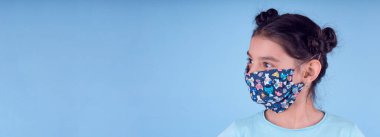 Renkli maskeli komik kız. Heyecan ve cazibe konsepti. Coronavirus mavi arka plan. Aptalca somurtmalar komik çılgın jestler. Komik bir ifade. Covid-19. panorama arkaplanı