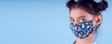 Renkli maskeli komik kız. Heyecan ve cazibe konsepti. Coronavirus mavi arka plan. Aptalca somurtmalar komik çılgın jestler. Komik bir ifade. Covid-19. panorama arkaplanı