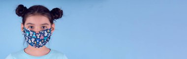 Renkli maskeli komik kız. Heyecan ve cazibe konsepti. Coronavirus mavi arka plan. Aptalca somurtmalar komik çılgın jestler. Komik bir ifade. Covid-19. panorama arkaplanı