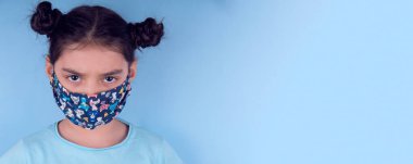 Renkli maskeli komik kız. Heyecan ve cazibe konsepti. Coronavirus mavi arka plan. Aptalca somurtmalar komik çılgın jestler. Komik bir ifade. Covid-19. panorama arkaplanı