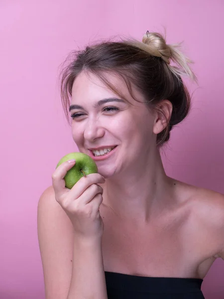 Pembe Arka Planda Yeşil Elma Yiyen Neşeli Genç Bir Kadının — Stok fotoğraf