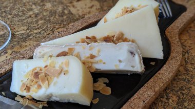 Peynir tabağı yakın plan. Tahta bir masa üzerinde çeşitli peynir tipleri ve bademlerle ahşap ve mermer tahta..