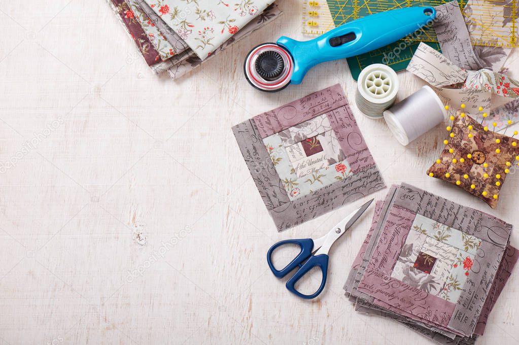 Patchwork log cabin blocks, stack of blocks, sewing accessories on white wooden surface