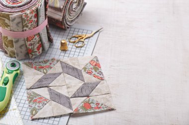 Patchwork blok zanaat mat üzerinde rulo kumaş, Beyaz ahşap yüzey üzerinde dikiş aksesuarları