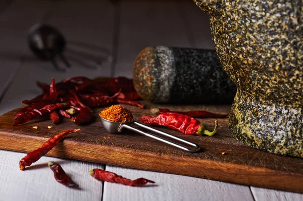 Measuring spoon with ground pepper on a chopping board, dried peppers, stone mortar and pestle
