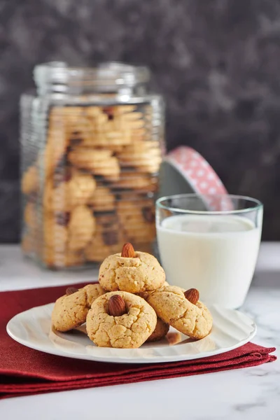Almond cookies on plate, glass of milk, jar with almond cookies