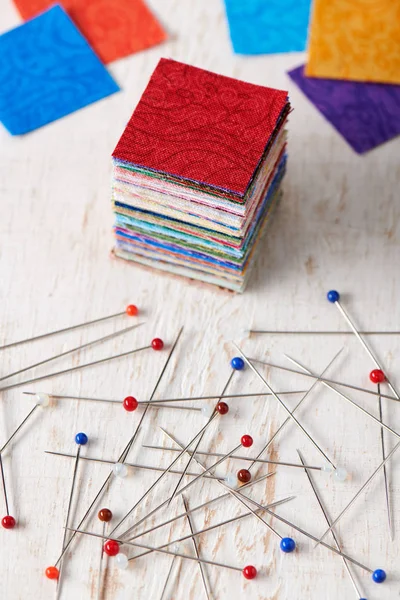 Stack of square pieces of colorful fabrics and heap of multicolor ball head sewing pins — Stock Photo, Image