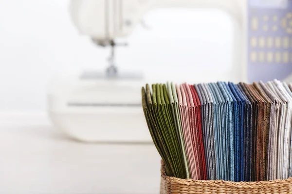 Στοίβα από πολύχρωμα υφάσματα για κουβερλί στο καλάθι στο φόντο της ραπτομηχανής — Φωτογραφία Αρχείου