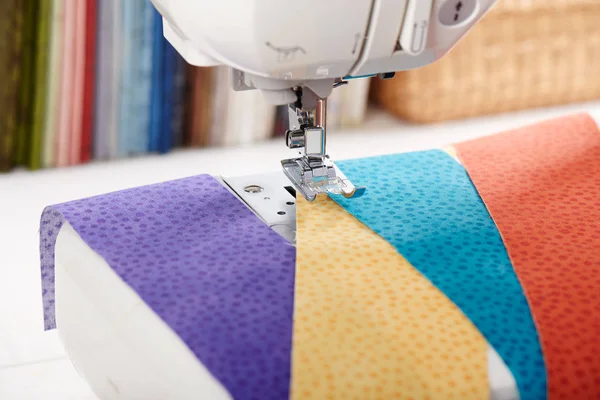 Швейная машина с полосками тканей на фоне стопки разноцветных стеганых тканей — стоковое фото