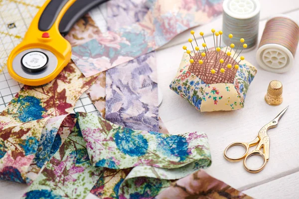 Strisce di tessuto dai colori vivaci, taglierina rotativa, cuscino perno e accessori trapuntatura su superficie in legno bianco — Foto Stock