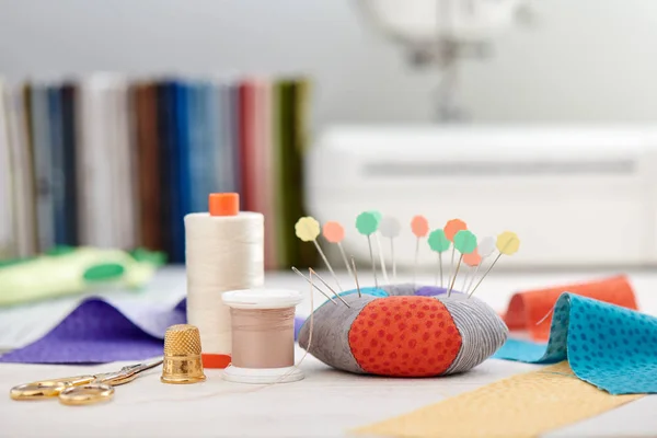 PIN kussen, felgekleurde strips van stof, naaien accessoires op de achtergrond van stapel stoffen en naaimachine — Stockfoto
