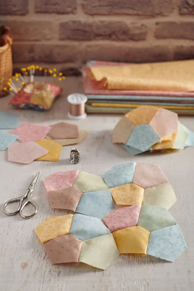 Stitched quilting blocks, piles of blocks and pentagons, stacks of fabrics, sewing accessories — Stock Photo, Image