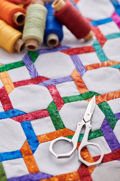 Schere und Garnspulen liegen auf einer Quiltplatte, die von Hand aus geometrischen Figuren genäht wurde — Stockfoto