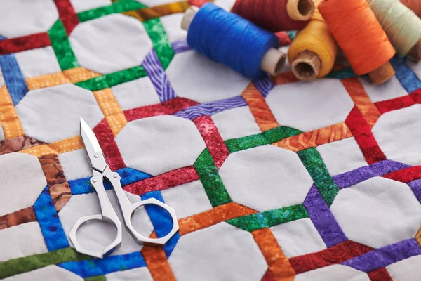 Schaar en spoelen van draad liggend op fragment quilt top genaaid met de hand van geometrische figuren — Stockfoto