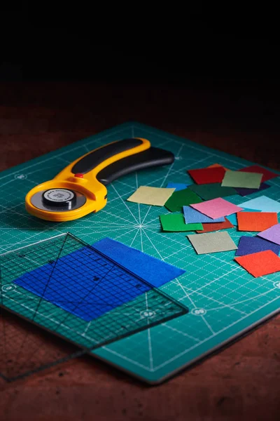 Heap vierkante stukken van kleurrijke stoffen, roterende cutter en liniaal op snijden mat — Stockfoto