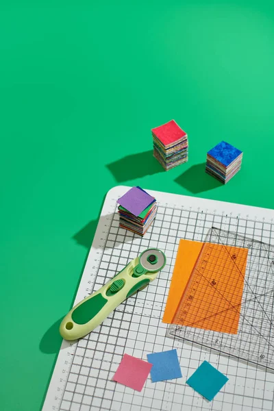 旋转切割机,尺子,明亮的方形织物件,工艺垫上一叠明亮的方形织物件,绿色背景 — 图库照片