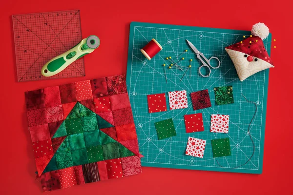 Julgran lapptäcke block, hantverk matta, ljusa kvadratiska bitar av tyg, pincushion som Santa och quiltning tillbehör på röd bakgrund — Stockfoto