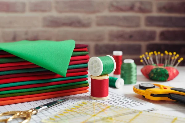 Stapel van rode en groene stoffen omgeven door naaien en quilten accessoires op bakstenen muur achtergrond — Stockfoto
