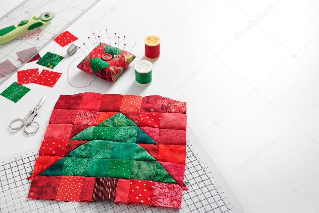 Christmas tree patchwork block, bright square pieces of fabric, pincushion, quilting and sewing accessories on white background