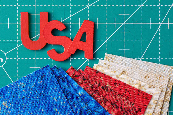 Wooden letters consisting to the abbreviation USA and square pieces of fabric in the US flag colors on a green craft mat