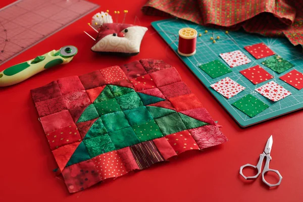 Blocco patchwork albero di Natale, stuoia mestiere, pezzi quadrati luminosi di tessuto, puntaspilli come Babbo Natale e accessori trapuntatura su sfondo rosso — Foto Stock