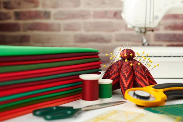 Stapel van rode en groene stoffen, naaien en quilten accessoires en naaimachine op bakstenen muur achtergrond — Stockfoto