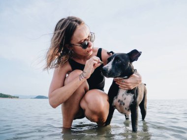 Genç Kafkasyalı kız komuta köpeğini eğitiyor sığ deniz kıyısında duruyor.