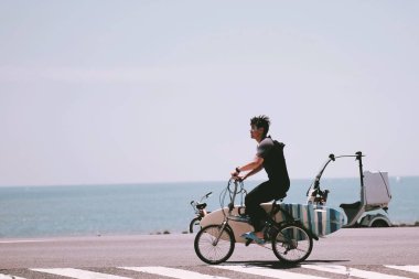 Denizde sörf yapmak için bisiklete binen genç bir adam.