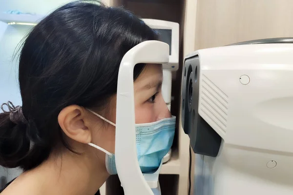 Asian women with surgical mask and optometrist examining eyesight patient in optician office