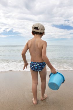 deniz kıyısında mavi kova ile oynayan şapkalı küçük çocuk