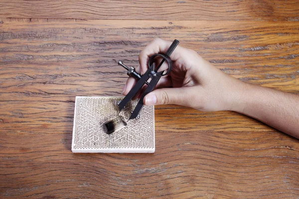 Hand holds a goldsmiths tools on the jewelry workplace. Jeweler at work in jewelry. Craft jewelry making with professional tool over wooden background