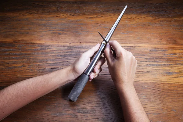 Hand holds a goldsmiths tools on the jewelry workplace. Jeweler at work in jewelry. Craft jewelry making with professional tool over wooden background