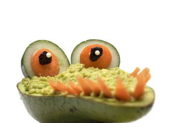 Yaratıcı timsah daldırma ile avokado yapılmış, salatalık gözleri ve beyaz arka plan üzerinde izole havuç yapılmış dişler