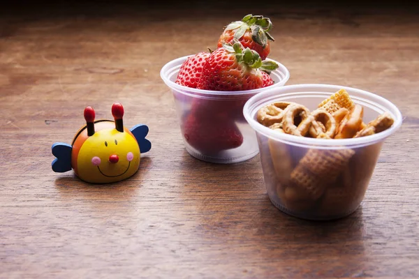 School lunch box snacks for kids over wooden background. Back to school. Healthy and fun snack option for moms. Cute food art creative concepts. Bowl with fruits and pretzel and cute wooden toy.