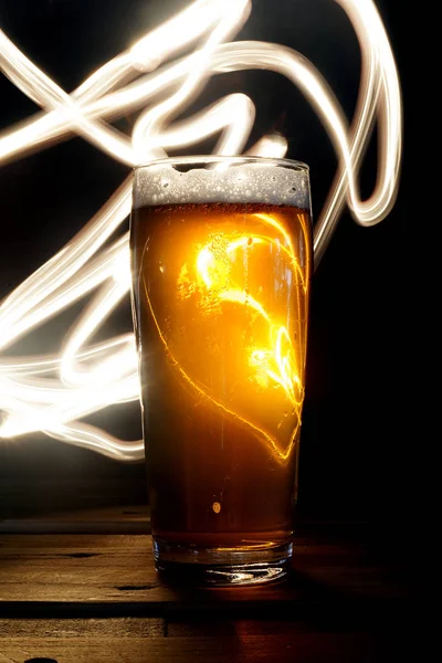Close up Beer Glass with Light painting background. Amazing abstract colored lights in motion. Magical light in a glass of craft beer.